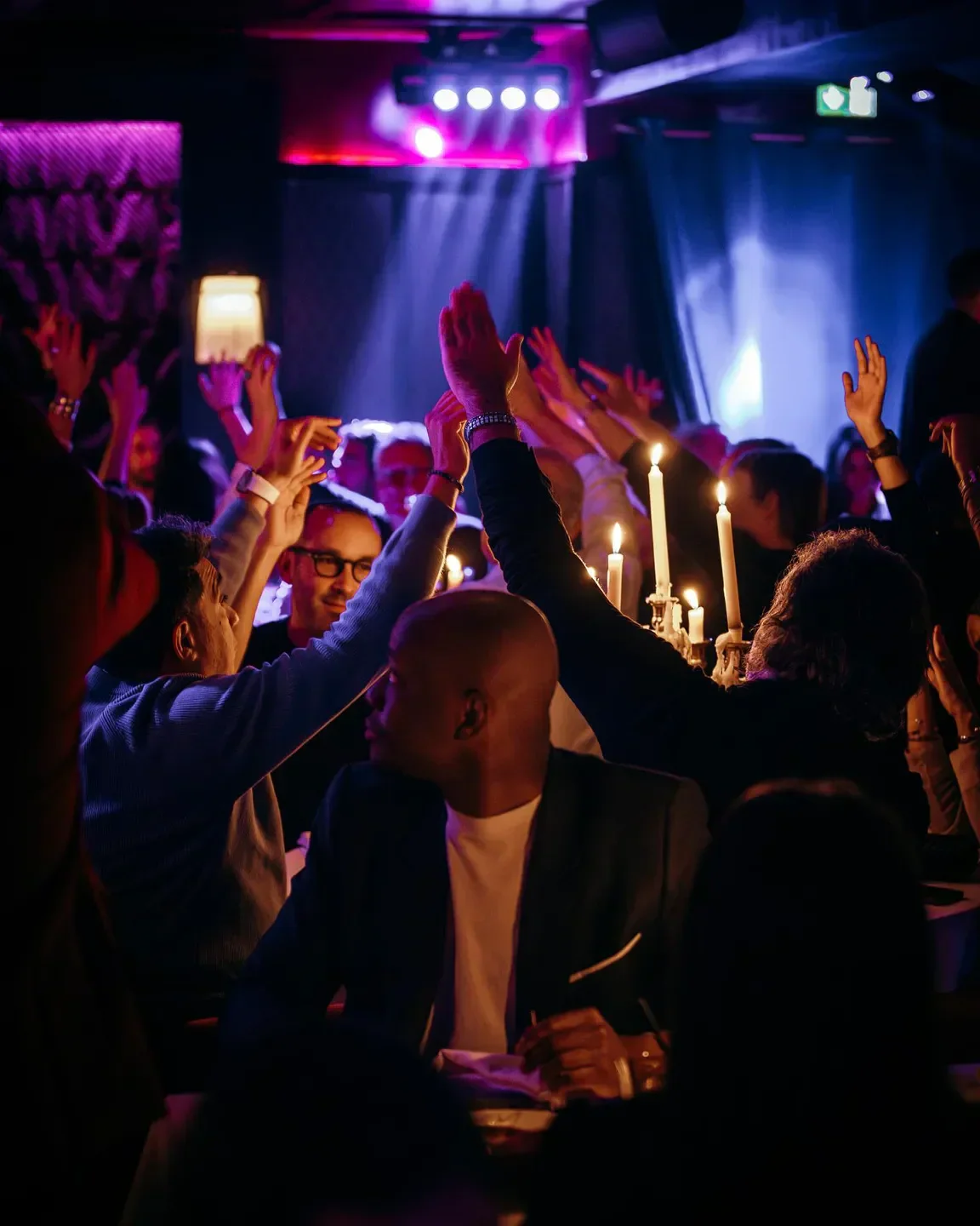 Celebratory atmosphere at La Mangeoire restaurant in Courchevel, with raised hands and candlelight.