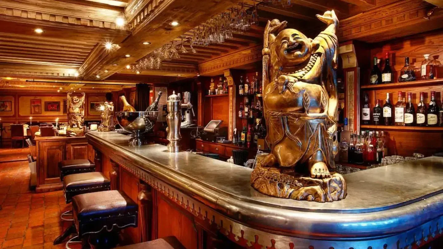 Interior of Le Café in Courchevel with bar, stools, and Buddha statue decor.